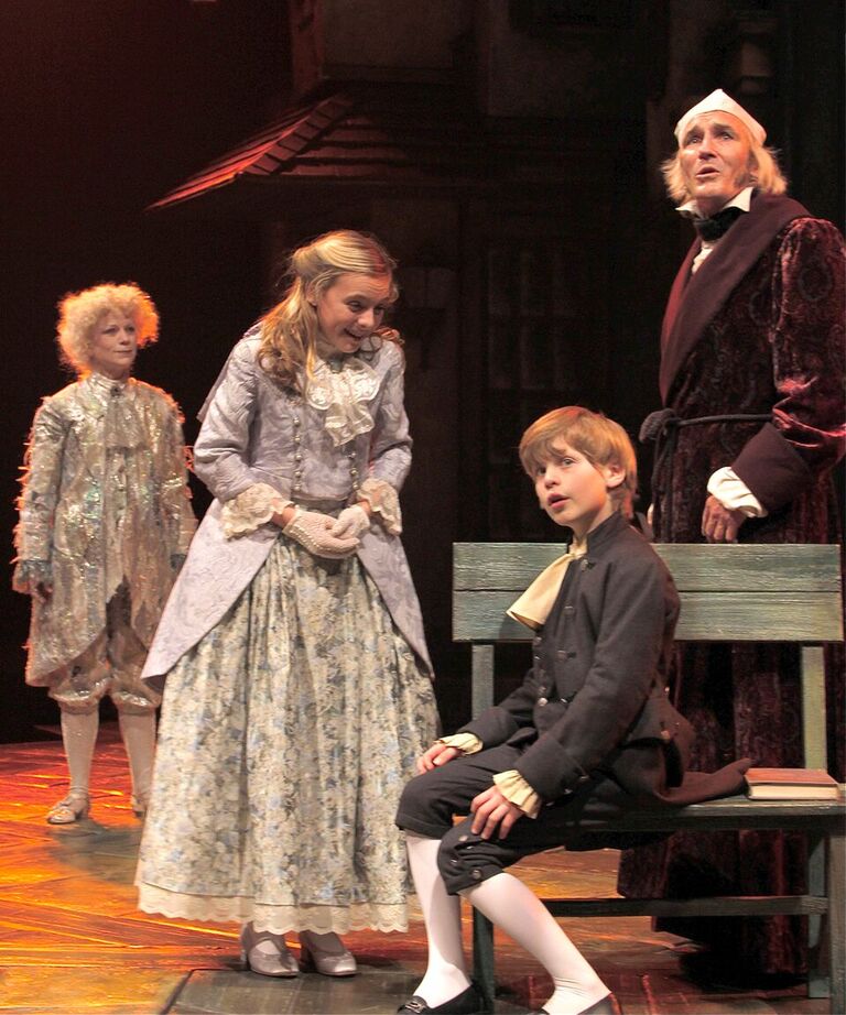 Allison Edwards (Fan, second from left) greets Ethan Verderber (Boy Scrooge, second from right) as Raye Lankford (Ghost of Christmas Past, left) and Bruce Cromer (Ebenezer Scrooge, right) observe in the 2013 production.
